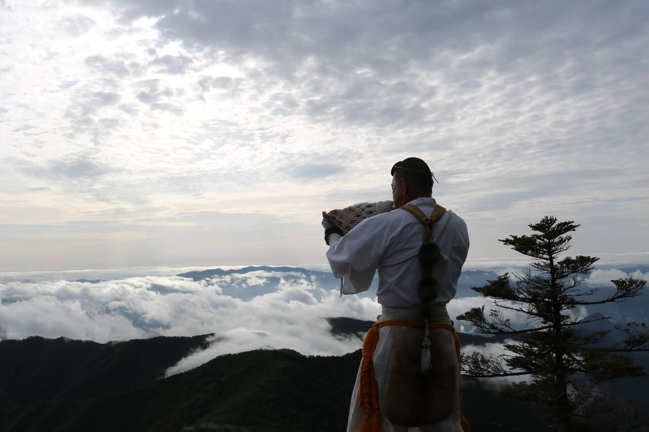 弥山からの雲海の前で法螺を吹く山伏ガイド上野さん